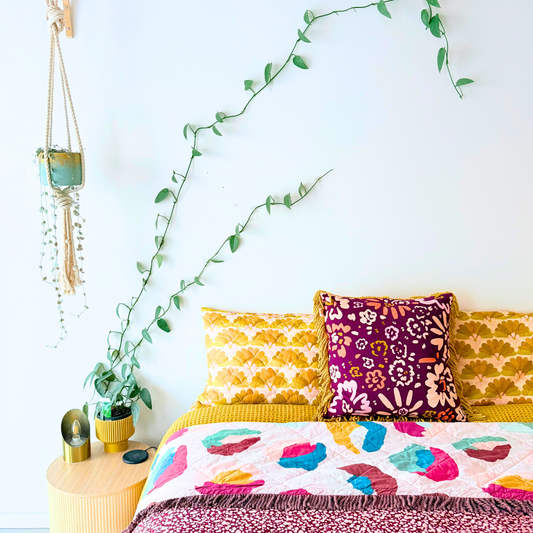 Colourful bed with pathos ivy growing up walls above the bed. Hanging plant in teal and gold pot hanging from wall with variegated plant trailing down