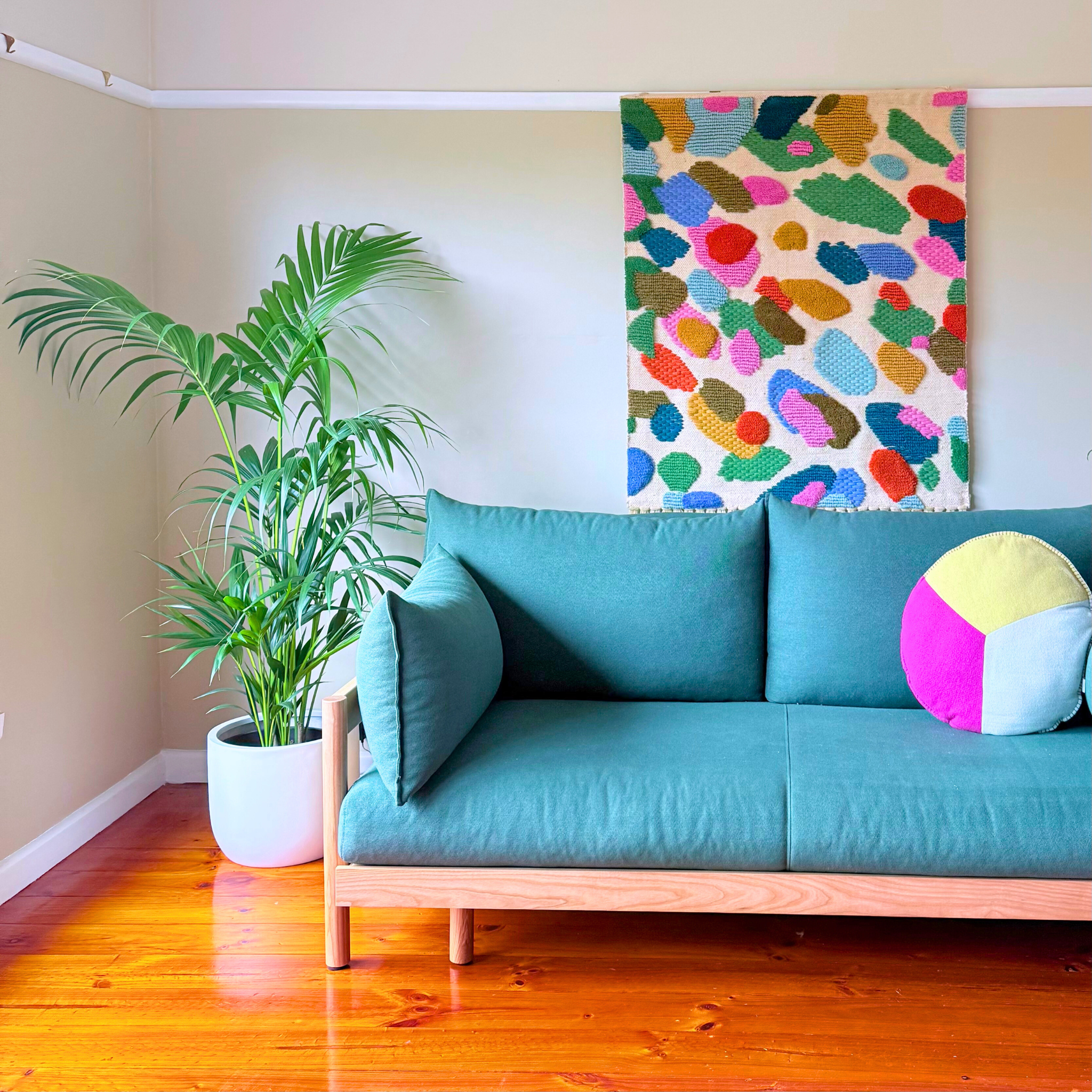 Turquoise sofa with colorful pillow in a room with a Kentia Palm plant and abstract wall art.