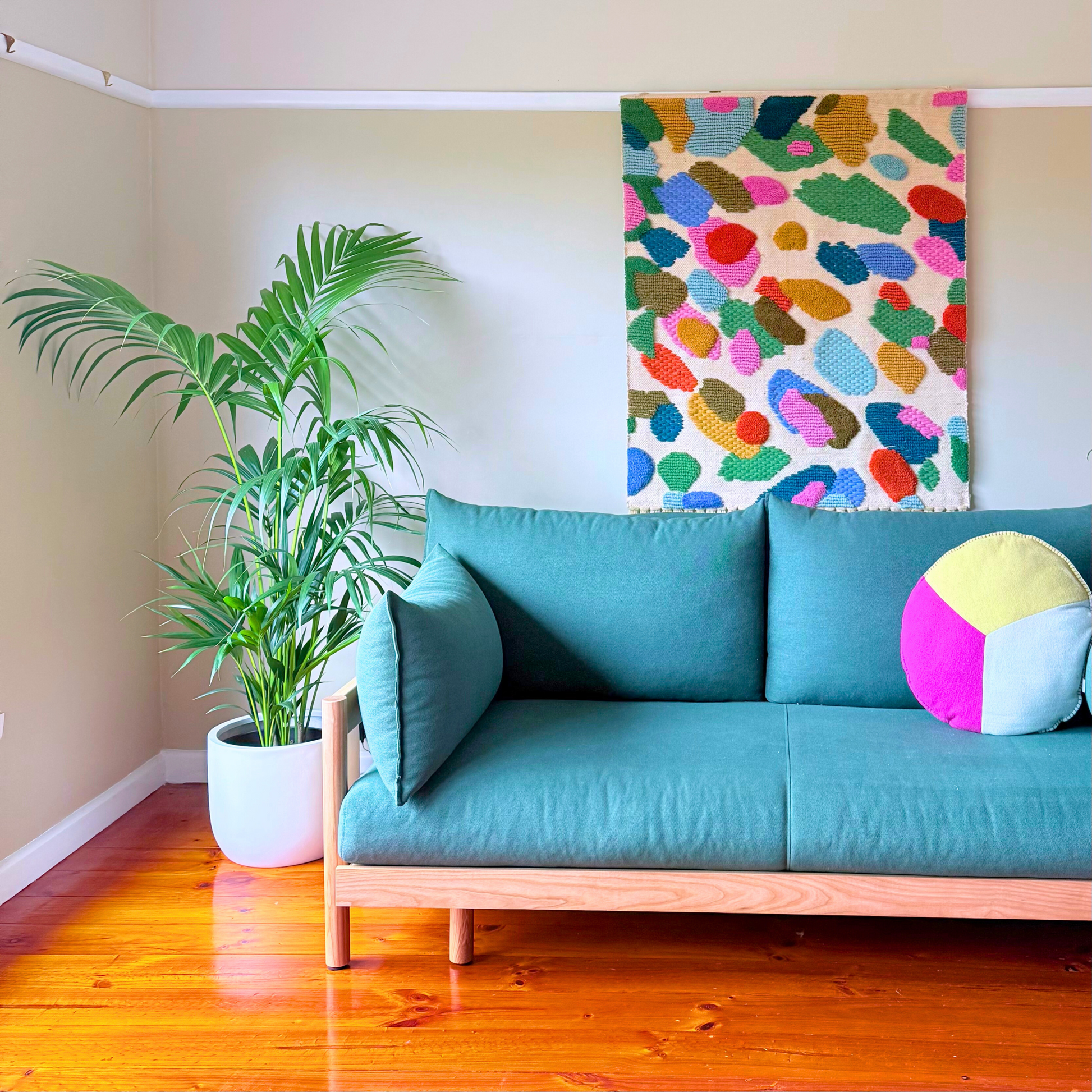 Turquoise sofa with colorful pillow in a room with a Kentia Palm plant and abstract wall art.